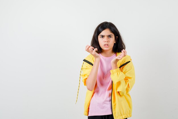 Портрет девочки-подростка, держащей руки возле лица в футболке, куртке и смотрящей сердитый вид спереди