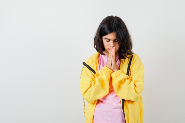 Tシャツ、黄色のジャケットで祈りのジェスチャーで手をつないで、焦点を絞った正面図を探している10代の少女の肖像画