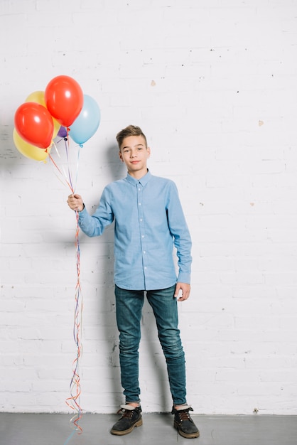 Portrait of teenage boy holding colorful balloons in hand