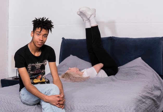 Free photo portrait of a teenage boy sitting on bed and her girlfriend lying on bed at background