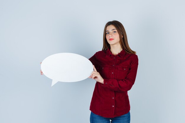 Portrait of teenage girl holding speech bubble in burgundy shirt and looking confident front view