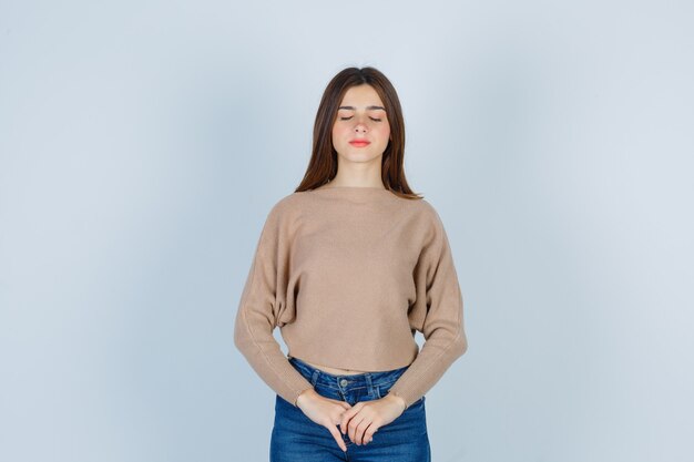 Portrait of teenage girl keeping eyes shut in sweater, jeans and looking dreamy front view