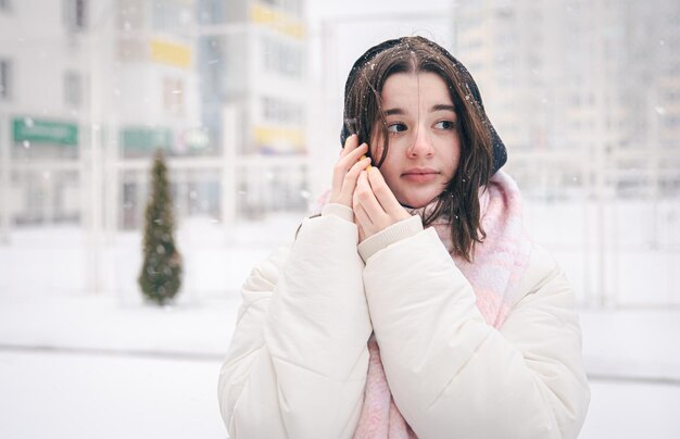 雪の降る冬の天候でスマートフォンを持って屋外で10代の少女の肖像画