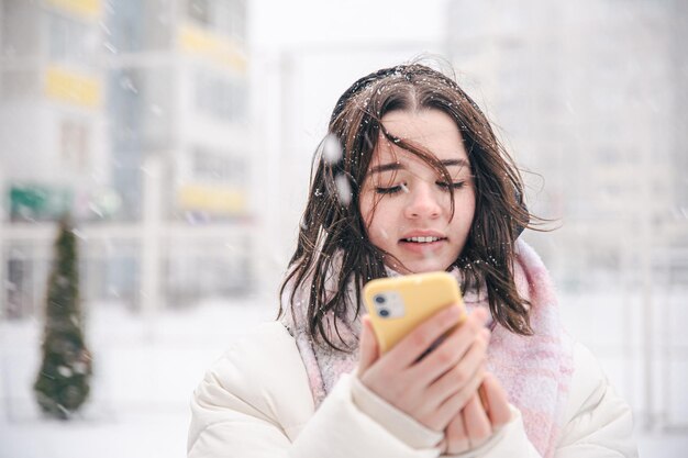 雪の降る冬の天候でスマートフォンを持って屋外で10代の少女の肖像画