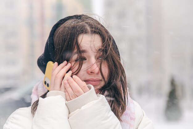 Портрет девочки-подростка на улице со смартфоном в снежную зимнюю погоду