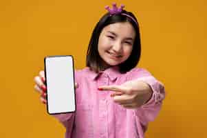Free photo portrait of a teenage girl showing her smartphone and pointing at it