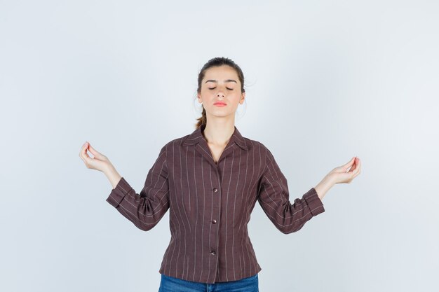 Portrait of teenage girl showing mudra gesture, shutting eyes in brown striped shirt and looking relaxed front view