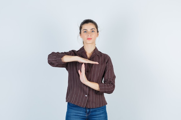 Foto gratuita ritratto di un'adolescente che mostra un gesto di pausa temporale con una camicia a righe marrone e sembra una vista frontale sicura