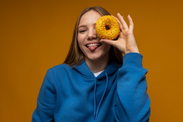 Foto gratuita ritratto di una ragazza adolescente che tira fuori la lingua e guarda attraverso una ciambella