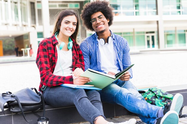 キャンパスに座って本を手で保持している10代の男性と女性の学生の肖像画