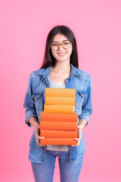 Portrait teenage pretty girl holding stack of books and smiley on pink, education teenge concept