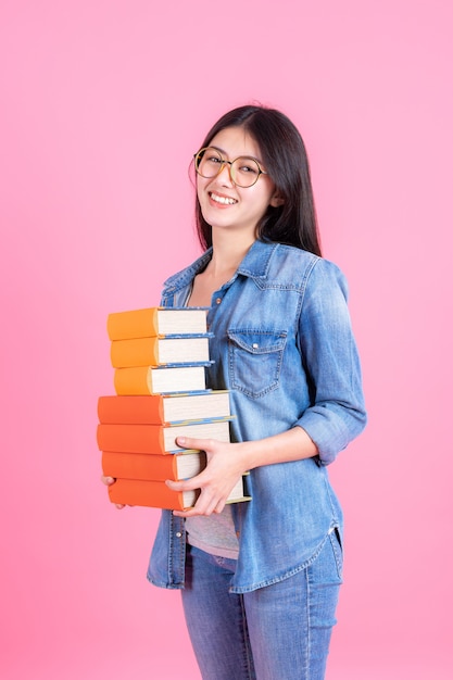 Free photo portrait teenage pretty girl holding stack of books and smiley on pink, education teenge concept