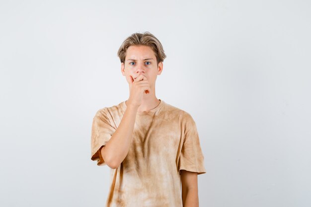 Portrait of teenager boy keeping hand on mouth in t-shirt and looking downcast front view