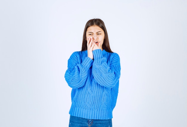 Portrait of teenager girl in blue sweater having toothache on white.