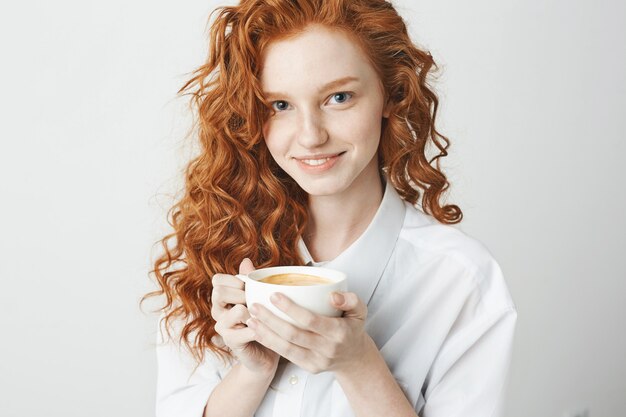 Portrait of tender redhead girl with freckles smiling holding cup