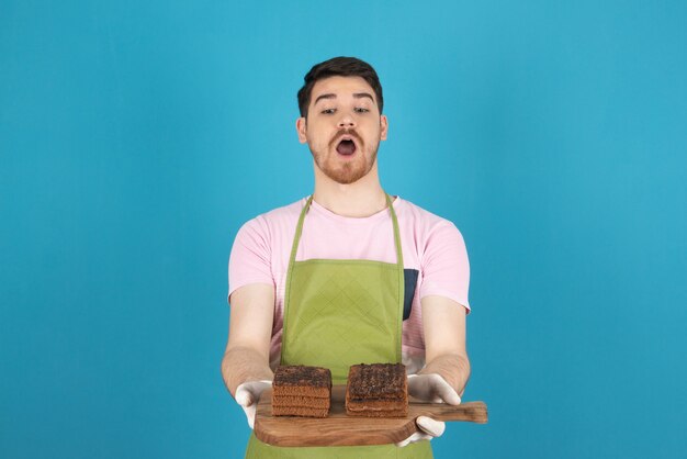 Portrait of terrified young man on a blue holding cake slices.