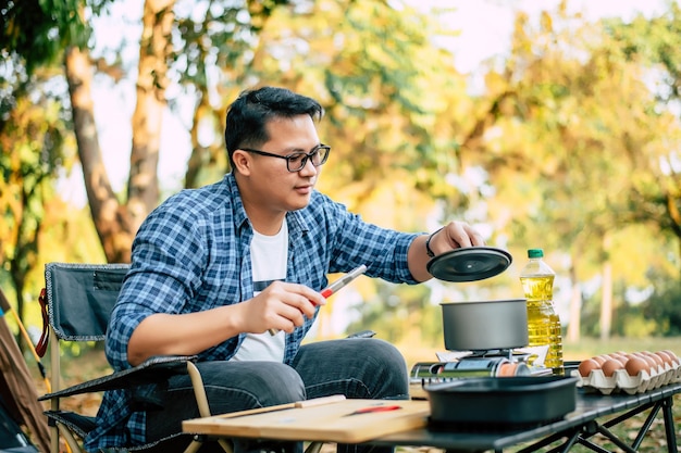 Portrait Thai traveler man glasses pouring sunflower oil into a frying pan Outdoor cooking traveling camping lifestyle concept