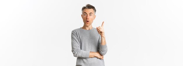 Portrait of thoughtful adult male model with short grey hair raising finger up having an idea say suggestion standing over white background