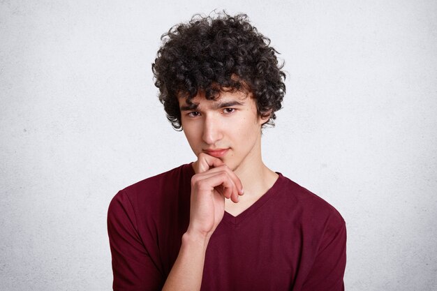 Portrait of thoughtful curly young male holds chin