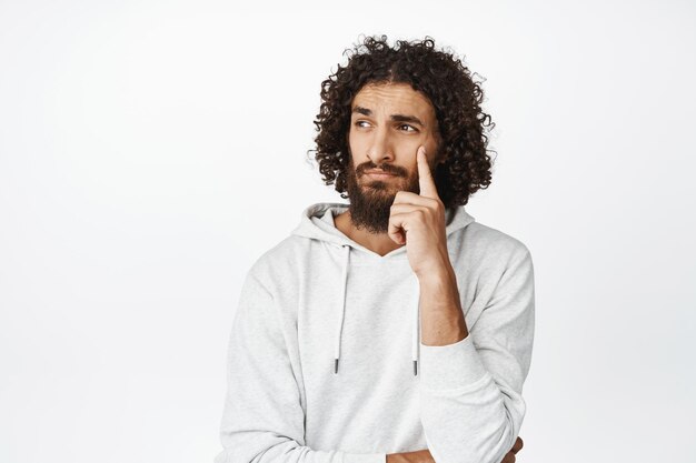 Portrait of thoughtful hispanic man looking aside pondering making decision or choosing standing over white background