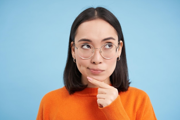 Foto gratuita il ritratto di una donna coreana premurosa con gli occhiali che pensa e guarda da parte ha un'idea che pianifica smth sta