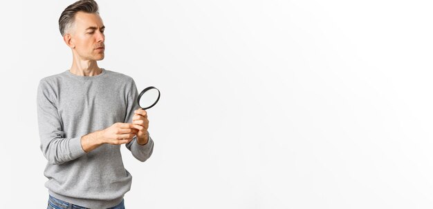 Free photo portrait of thoughtful middleaged man looking through magnifying glass searching for something or re