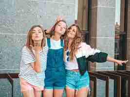 Foto gratuita ritratto di tre giovani belle ragazze sorridenti hipster in abiti estivi alla moda. donne spensierate sexy in posa sulla strada. divertimento di modelle positive. abbracciare e dare bacio d'aria