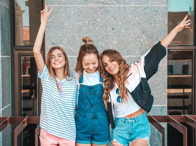 Портрет трех молодых красивых улыбающихся хипстерских девочек в модной летней одежде. Сексуальные беззаботные женщины позируют на улице. Позитивные модели с удовольствием. Обниматься и поднимать руки