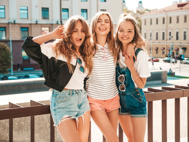 Portrait of three young beautiful smiling hipster girls in trendy summer clothes. Sexy carefree women posing on the street.Positive models having fun.Hugging and showing tongue