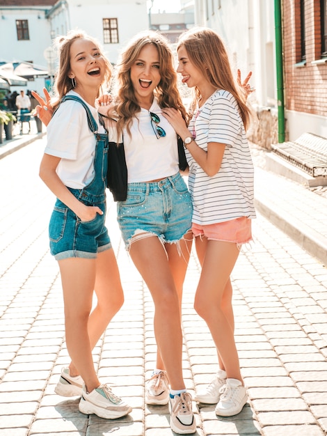 Foto gratuita ritratto di tre giovani belle ragazze sorridenti hipster in abiti estivi alla moda. donne spensierate sexy in posa sulla strada. divertimento di modelli positivi