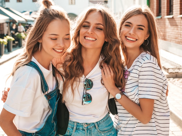 Ritratto di tre giovani belle ragazze sorridenti hipster in abiti estivi alla moda. donne spensierate sexy in posa sulla strada. divertimento di modelli positivi