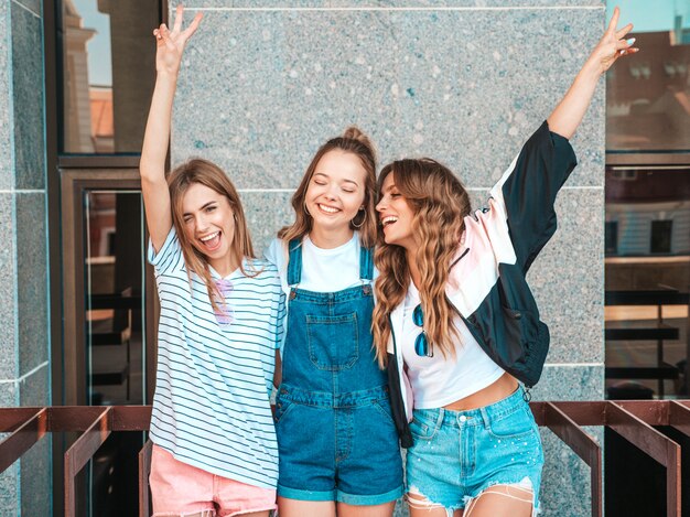 Портрет трех молодых красивых улыбающихся хипстерских девочек в модной летней одежде. Сексуальные беззаботные женщины позируют на улице. Позитивные модели с удовольствием. Поднимают руки