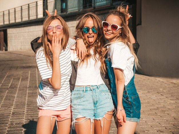 Portrait of three young beautiful smiling hipster girls in trendy summer clothes. Sexy carefree women posing the street.Positive models having fun in sunglasses.Hugging and showing tongue