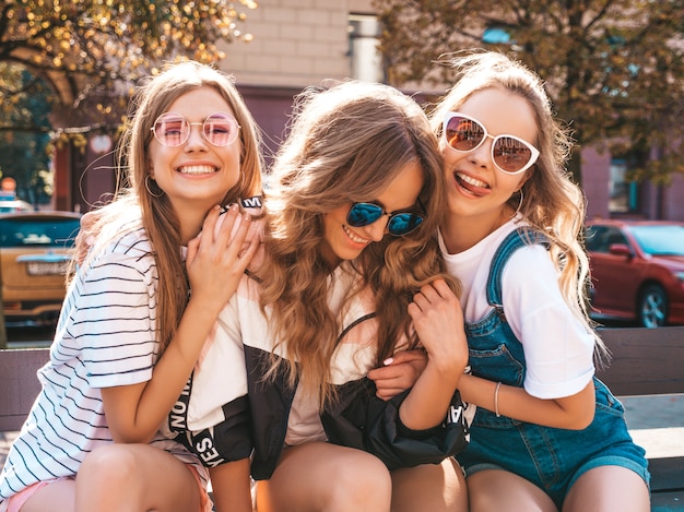 Portrait of three young beautiful smiling hipster girls in trendy summer clothes. Sexy carefree women posing on the street.Positive models having fun in sunglasses.Hugging