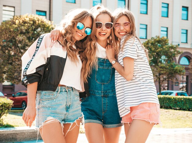 Portrait of three young beautiful smiling hipster girls in trendy summer clothes. Sexy carefree women posing on the street.Positive models having fun in sunglasses.Hugging