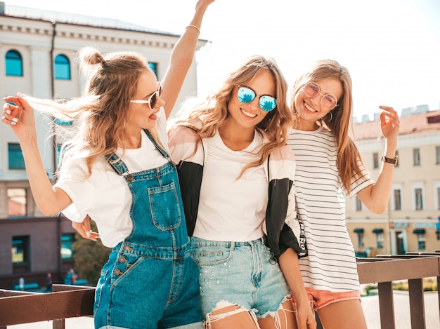 Foto gratuita ritratto di tre giovani belle ragazze sorridenti hipster in abiti estivi alla moda. donne spensierate sexy in posa sulla strada. modelli positivi che si divertono in occhiali da sole