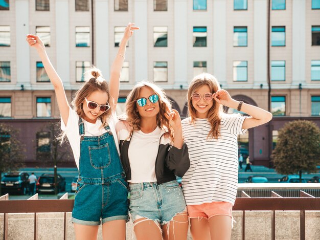 Портрет трех молодых красивых улыбающихся хипстерских девочек в модной летней одежде. Сексуальные беззаботные женщины позируют на улице. Позитивные модели веселятся в солнечных очках. Обнимаются
