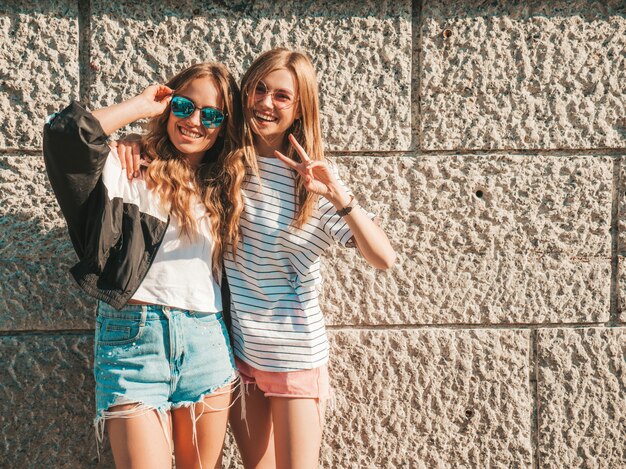 Портрет трех молодых красивых улыбающихся хипстерских девочек в модной летней одежде. Сексуальные беззаботные женщины позируют на улице. Позитивные модели веселятся в солнечных очках. Обнимаются