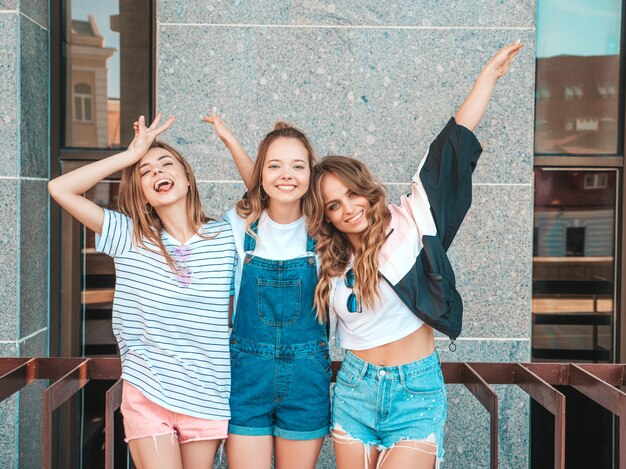 Портрет трех молодых красивых улыбающихся хипстерских девочек в модной летней одежде. Сексуальные беззаботные женщины позируют на улице. Позитивные модели веселятся. Они поднимают руки