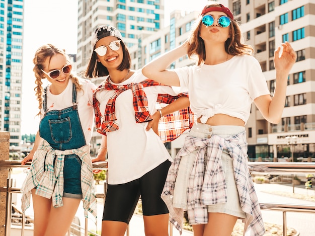 Portrait of three young beautiful smiling hipster girls in trendy summer clothes.