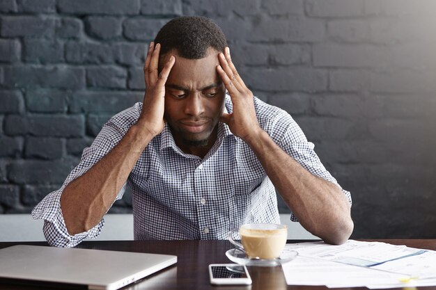 Portrait of tired exhausted young dark-skinned employee touching his head