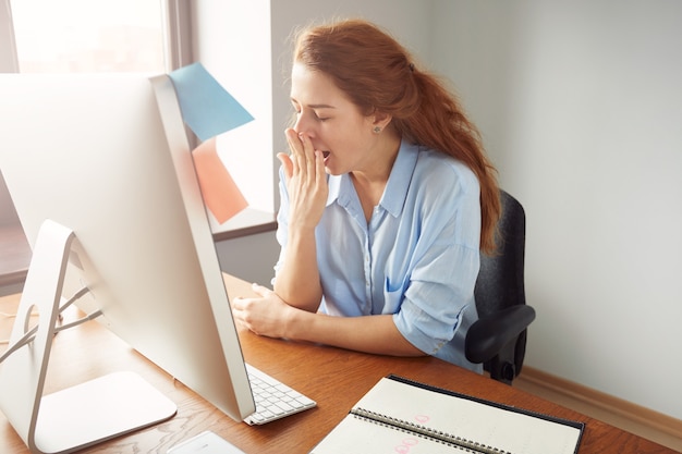 Ritratto di imprenditrice sonnolenta stanca che sbadiglia, lavorando alla scrivania in ufficio