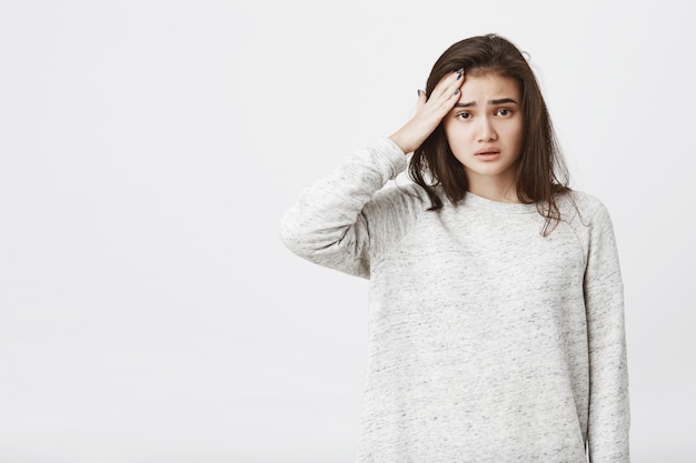 Free photo portrait of tired, unhappy european female model with frowned eyebrows and opened mouth, holding hand on forehead