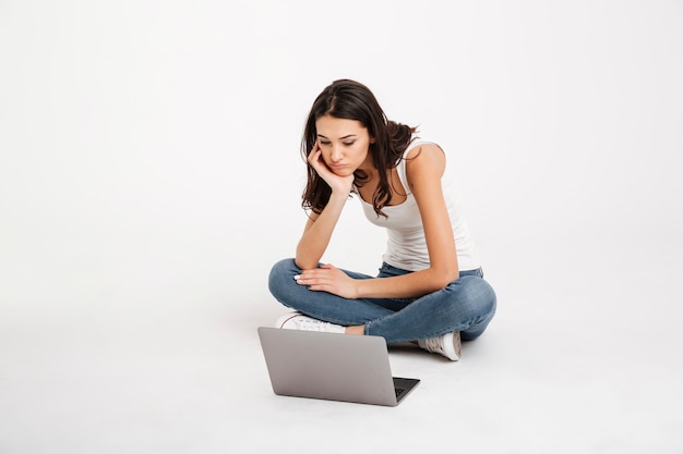Portrait of a tired woman dressed in tank-top holding laptop