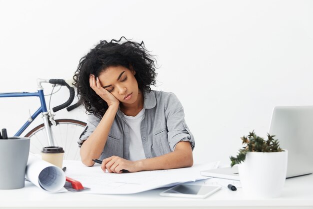 Portrait of tired young African American woman interior designer pillowing head on hand