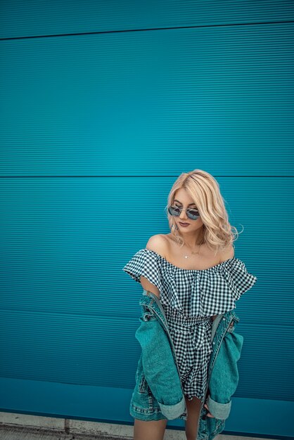 Portrait of Trendy Hipster Girl Standing at the blue turquoise wall Background. Urban Fashion Concept. Copy Space.