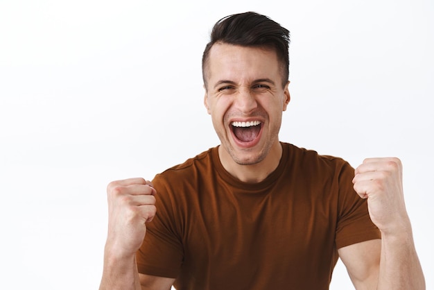 Portrait of triumphing handsome adult man chanting celebrating success or achievement clench fists and shouting yes with happy beaming smile winning prize become champion watching sports game