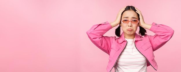 Portrait of troubled asian woman korean girl holds hands on head and look in panic standing distressed and shocked against pink background