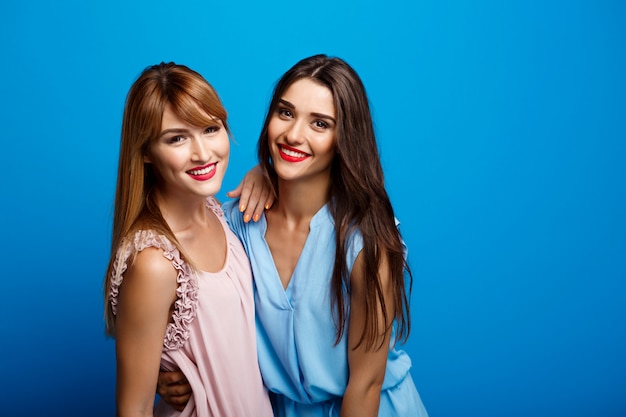 Portrait of two beautiful girls over blue wall