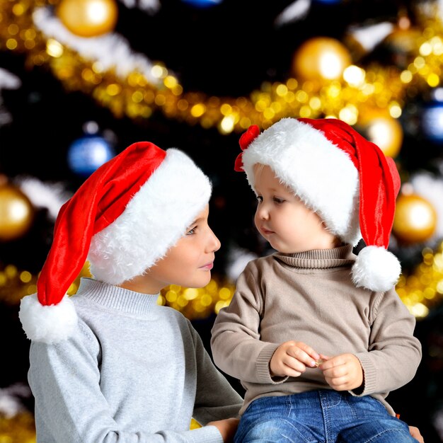 Portrait of two brothers in the new year Santa hats looking  at each other - indoor